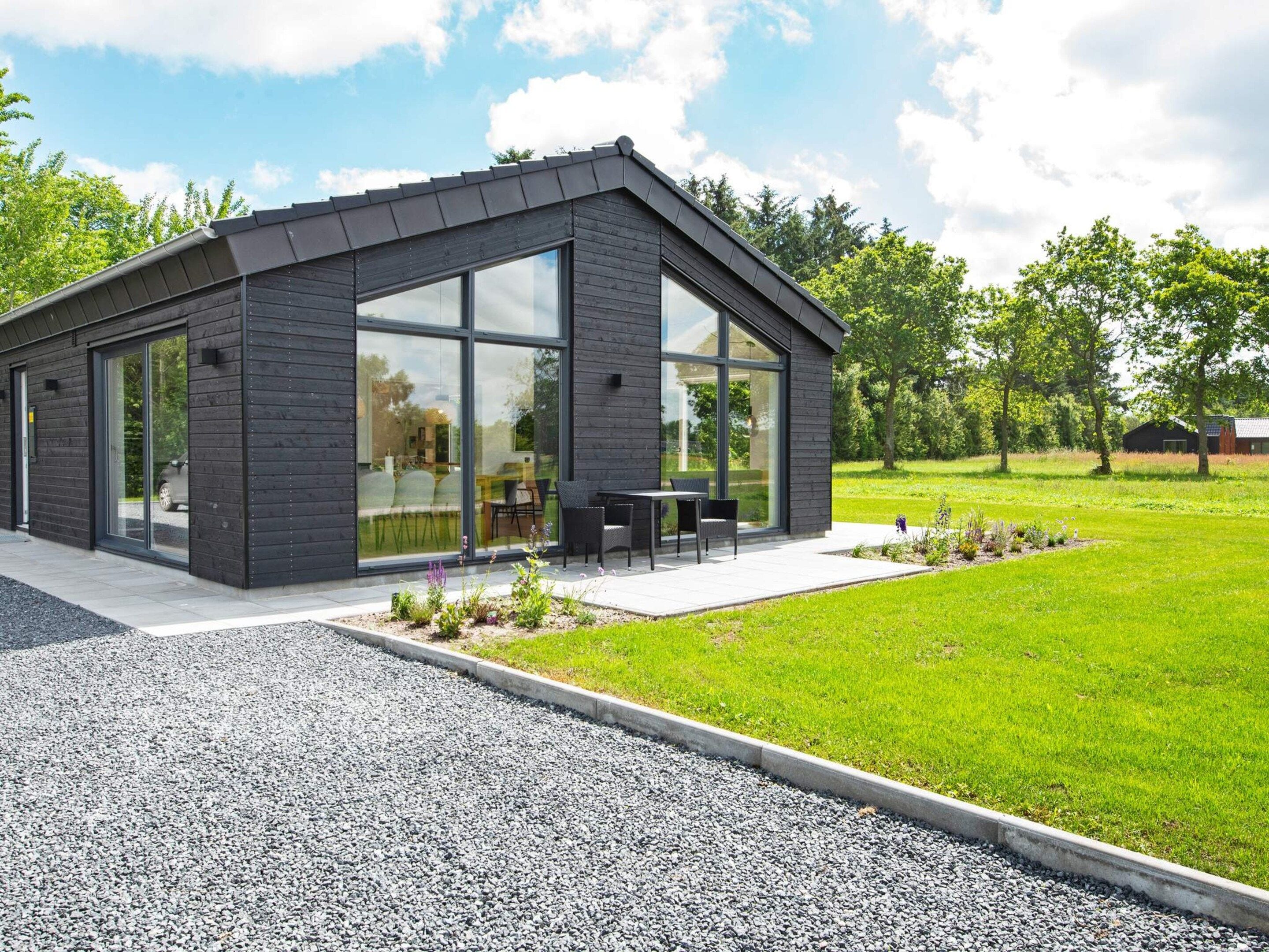 A modern building with large windows, a gravel driveway, and a grassy lawn.
