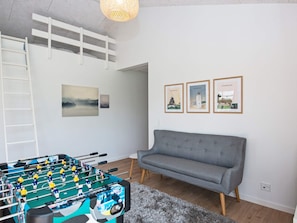 A room with a foosball table, a grey sofa, and three framed pictures on the wall.