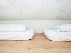 A room with two beds, wooden flooring, and a plain white ceiling.