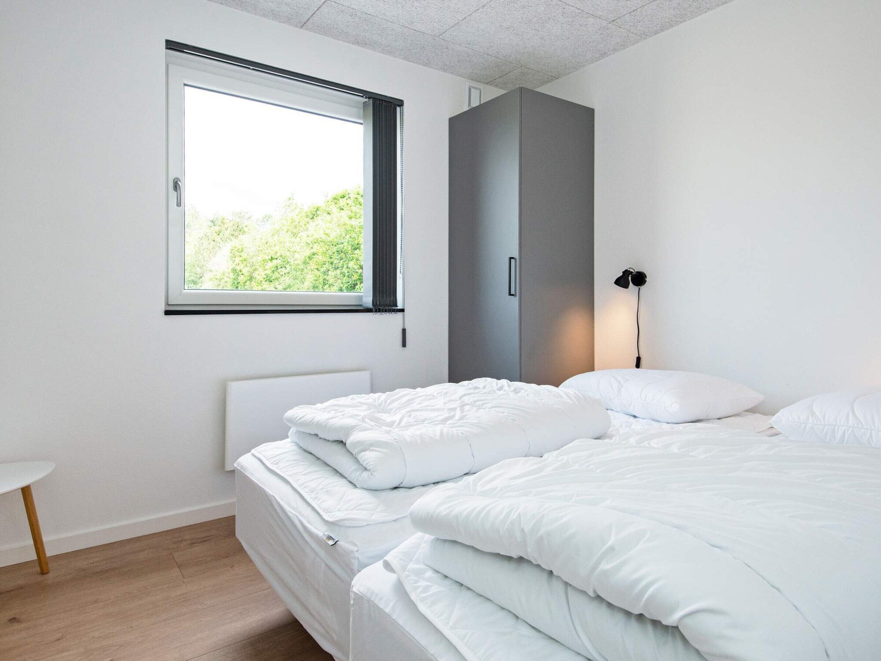 A modern bedroom with two beds, a window, a bedside lamp, and a small table.