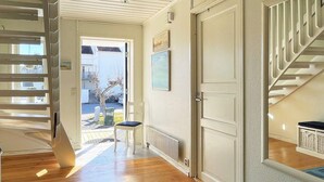 Um corredor com piso de madeira, uma porta branca, uma cadeira e uma escada com corrimãos brancos.
