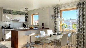 Uma cozinha moderna com armários brancos, uma ilha central e uma área de jantar com mesa e cadeiras.