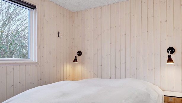 Quarto com cama, paredes de madeira, janela e duas luminárias fixadas na parede.
