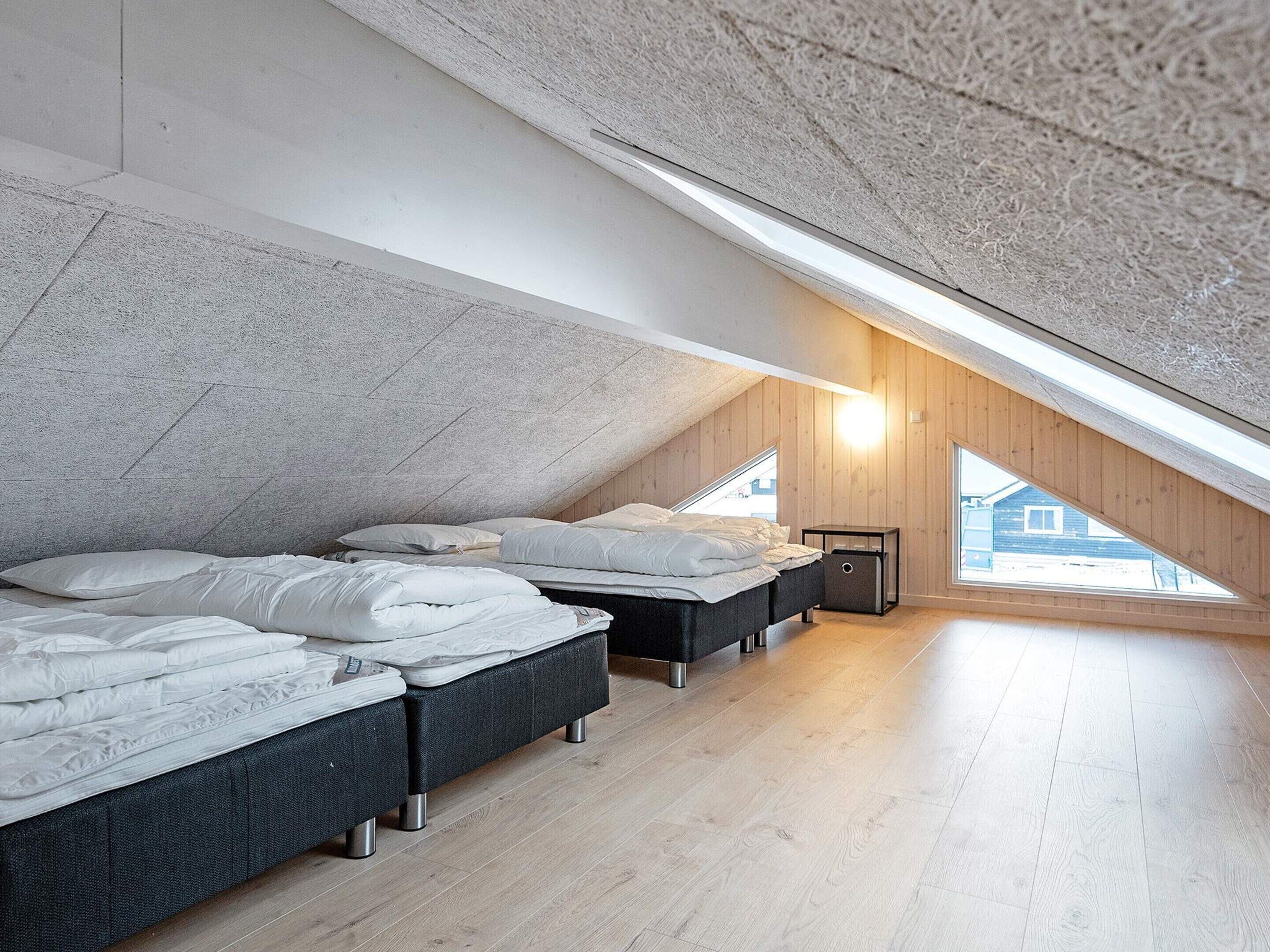 A bedroom with a sloped ceiling, two beds, a nightstand, and a window.