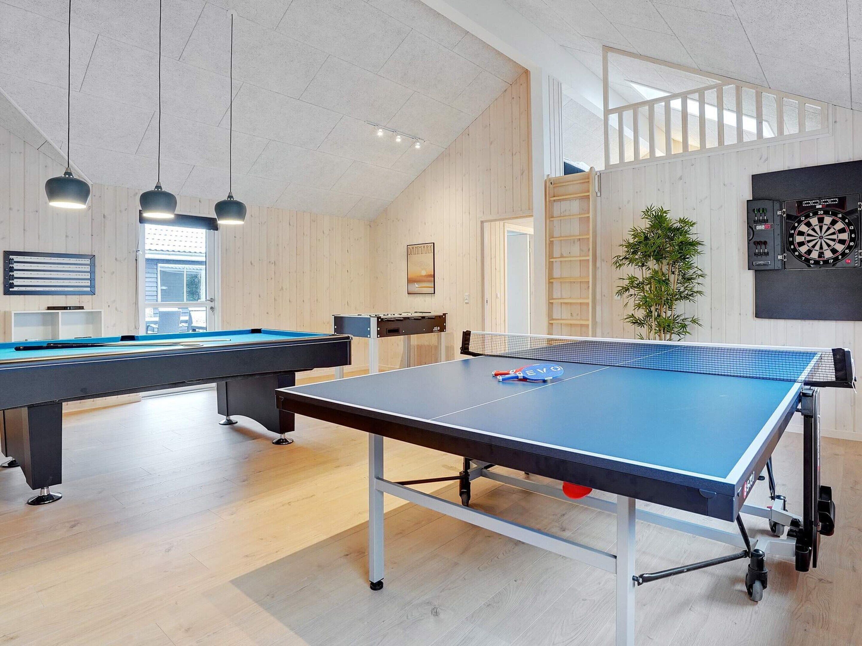 Een kamer met een tafeltennistafel, een pooltafel en een dartbord.