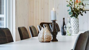 Mesa de jantar com cadeiras, uma vela, objetos decorativos e um vaso com folhagem.