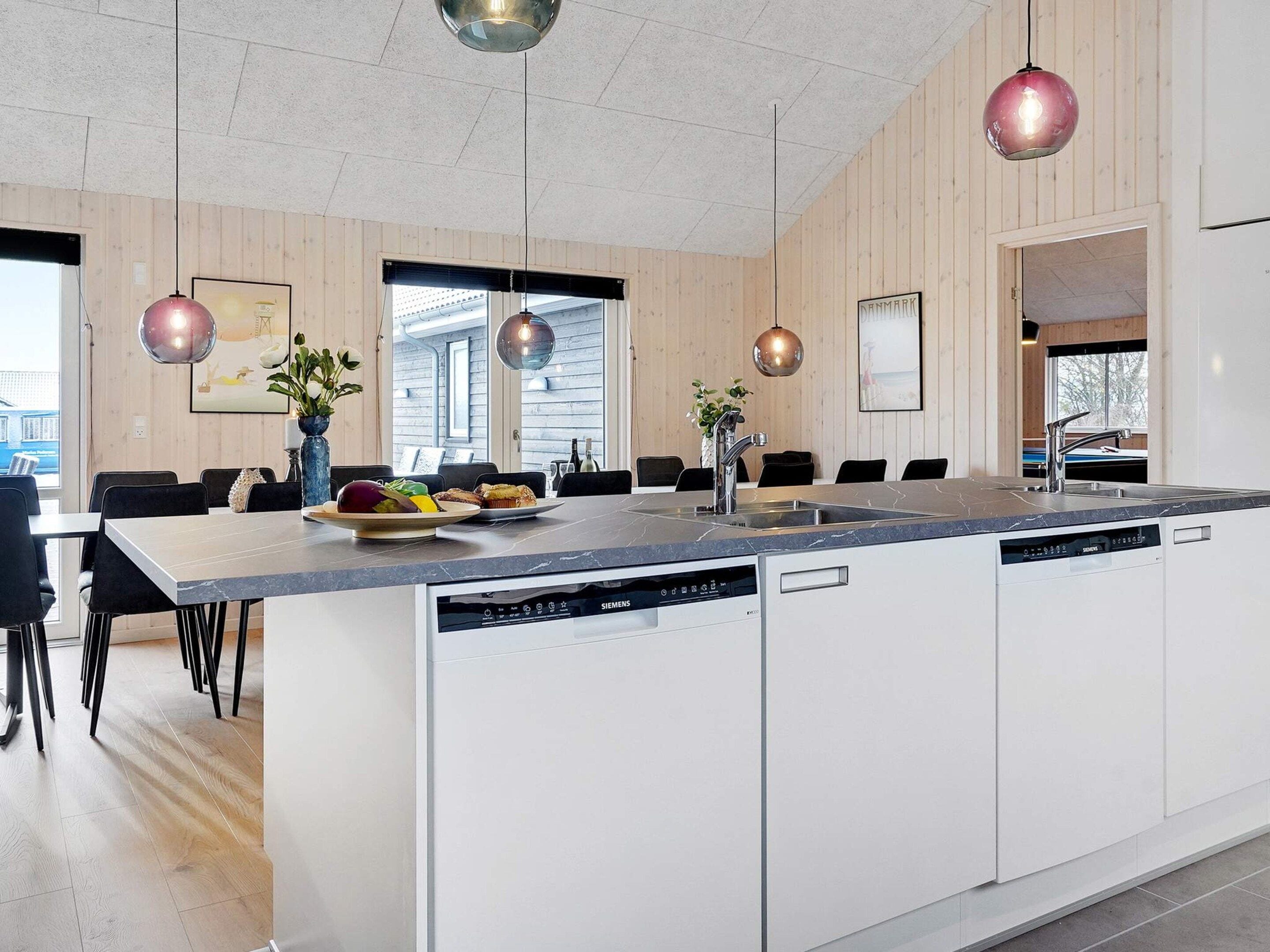 A modern kitchen with a central island, built-in dishwasher, and pendant lighting.