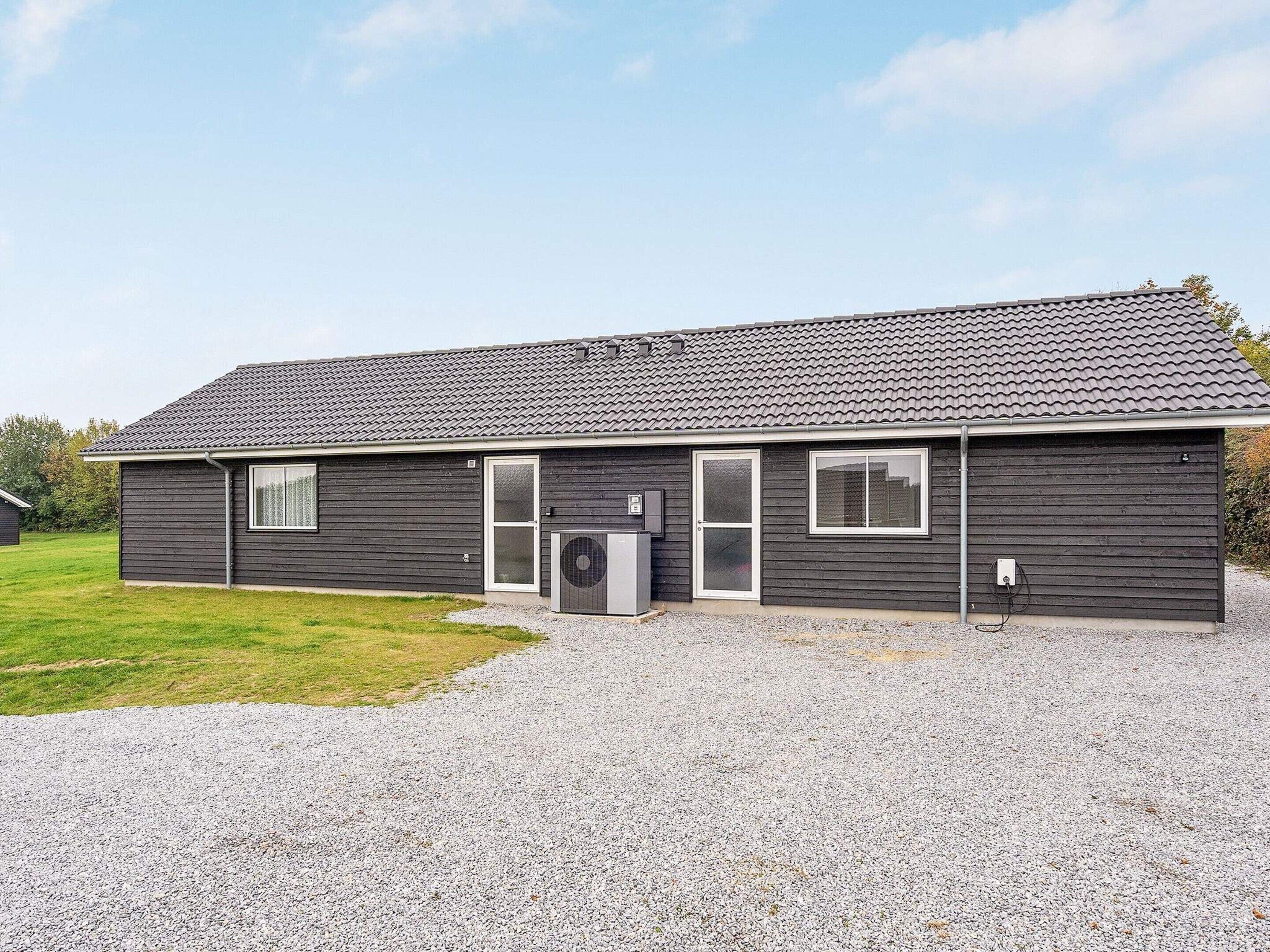 A single-story building with a dark exterior, a gravel driveway, and a clear sky.