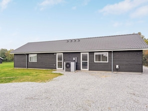 A single-story building with a dark exterior, a gravel driveway, and a clear sky.