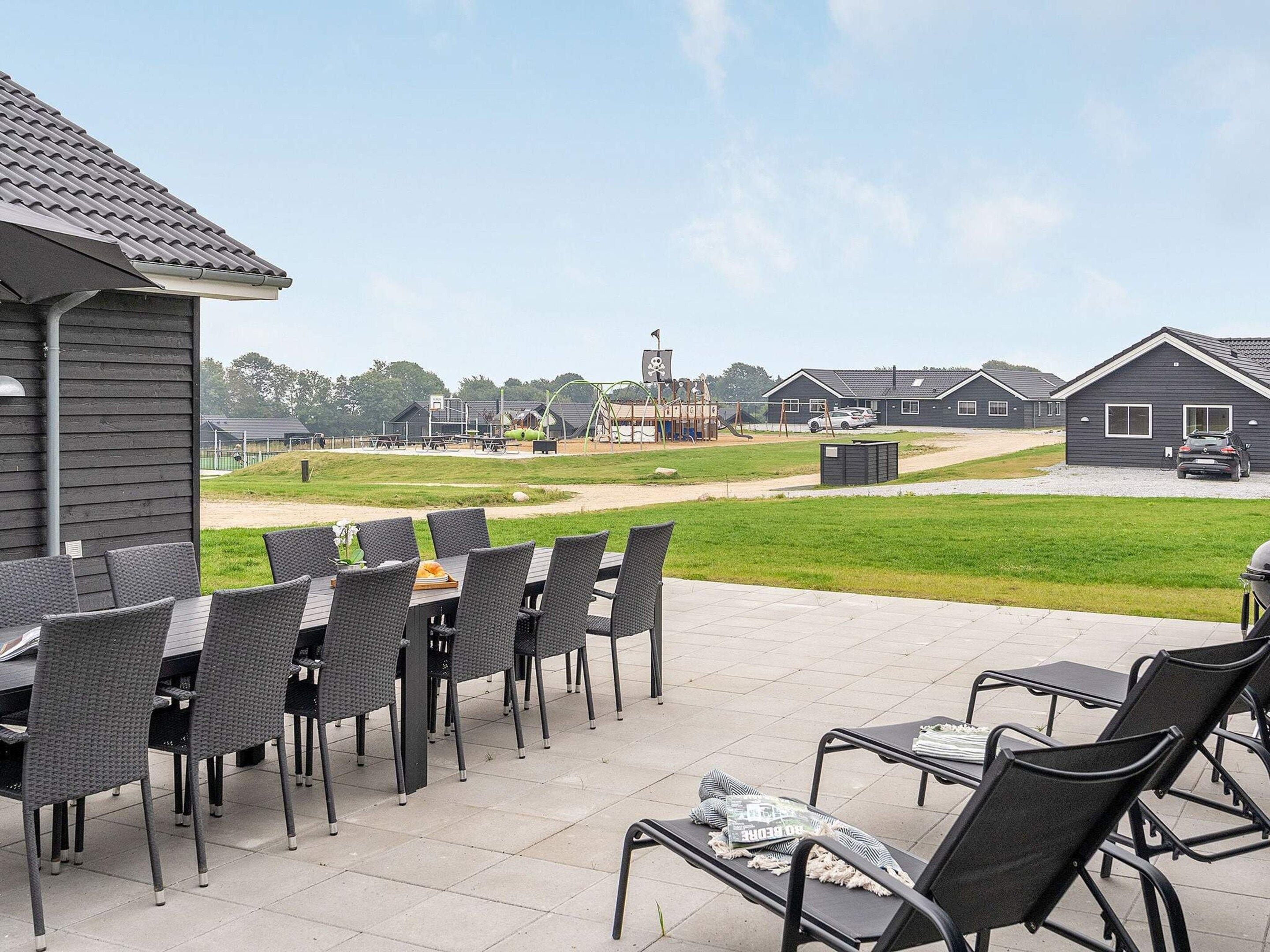 Une terrasse extérieure avec des tables et des chaises, une aire de jeux en arrière-plan et une rangée de maisons.