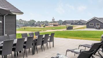 Een terras buiten met eettafels en stoelen, een speeltuin op de achtergrond en een rij huizen.