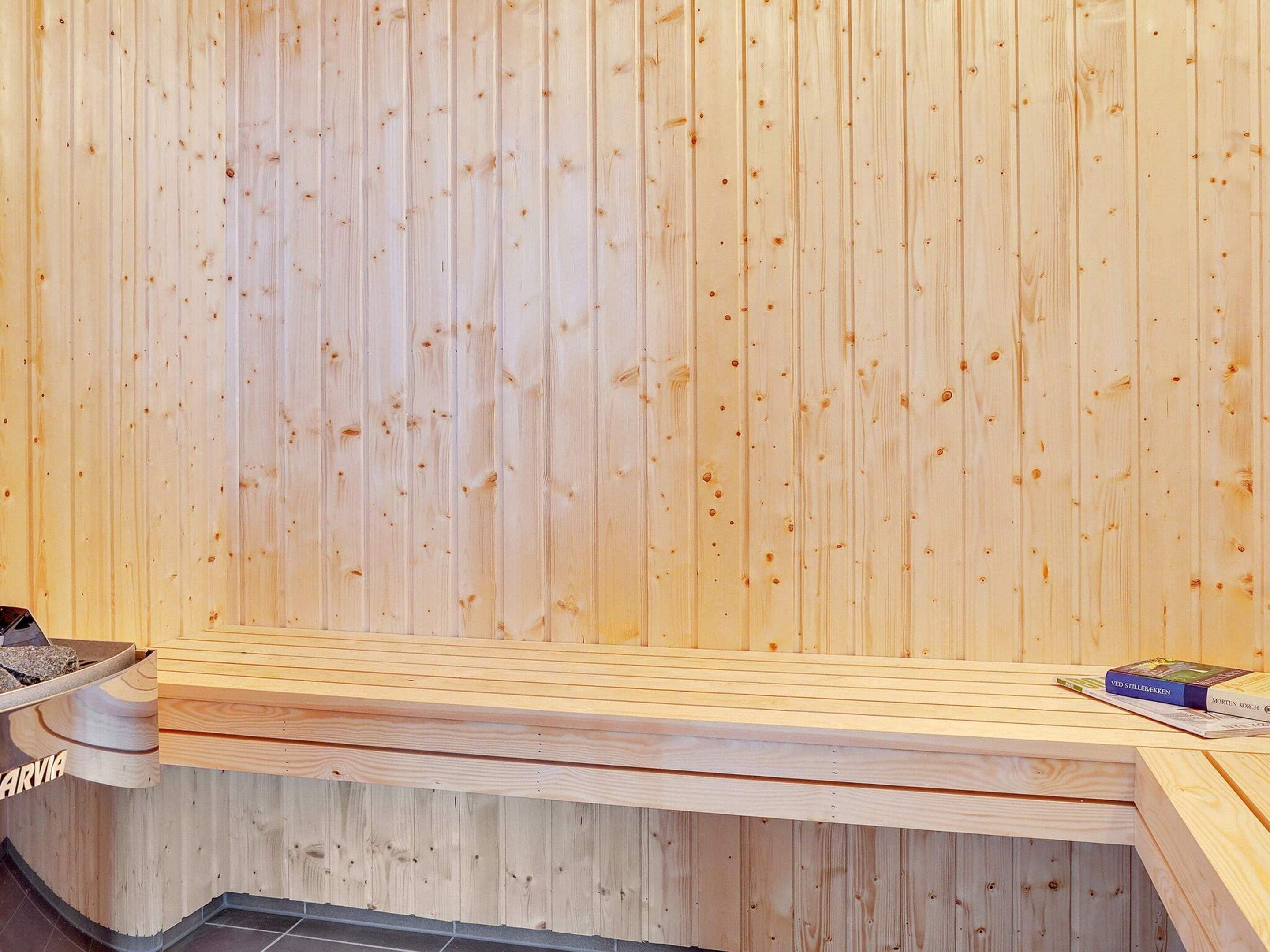 A sauna with a wooden bench and a small table with a book.