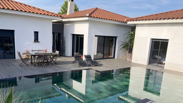 Una casa moderna con piscina cristalina, terraza de madera y zona de patio con mobiliario exterior.