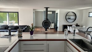 Una cocina moderna con una isla central, un comedor con una mesa redonda y una sala de estar con sofá y planta en maceta.