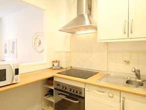 A kitchen with white cabinets, a stainless steel range hood, a microwave, an oven, and a sink.