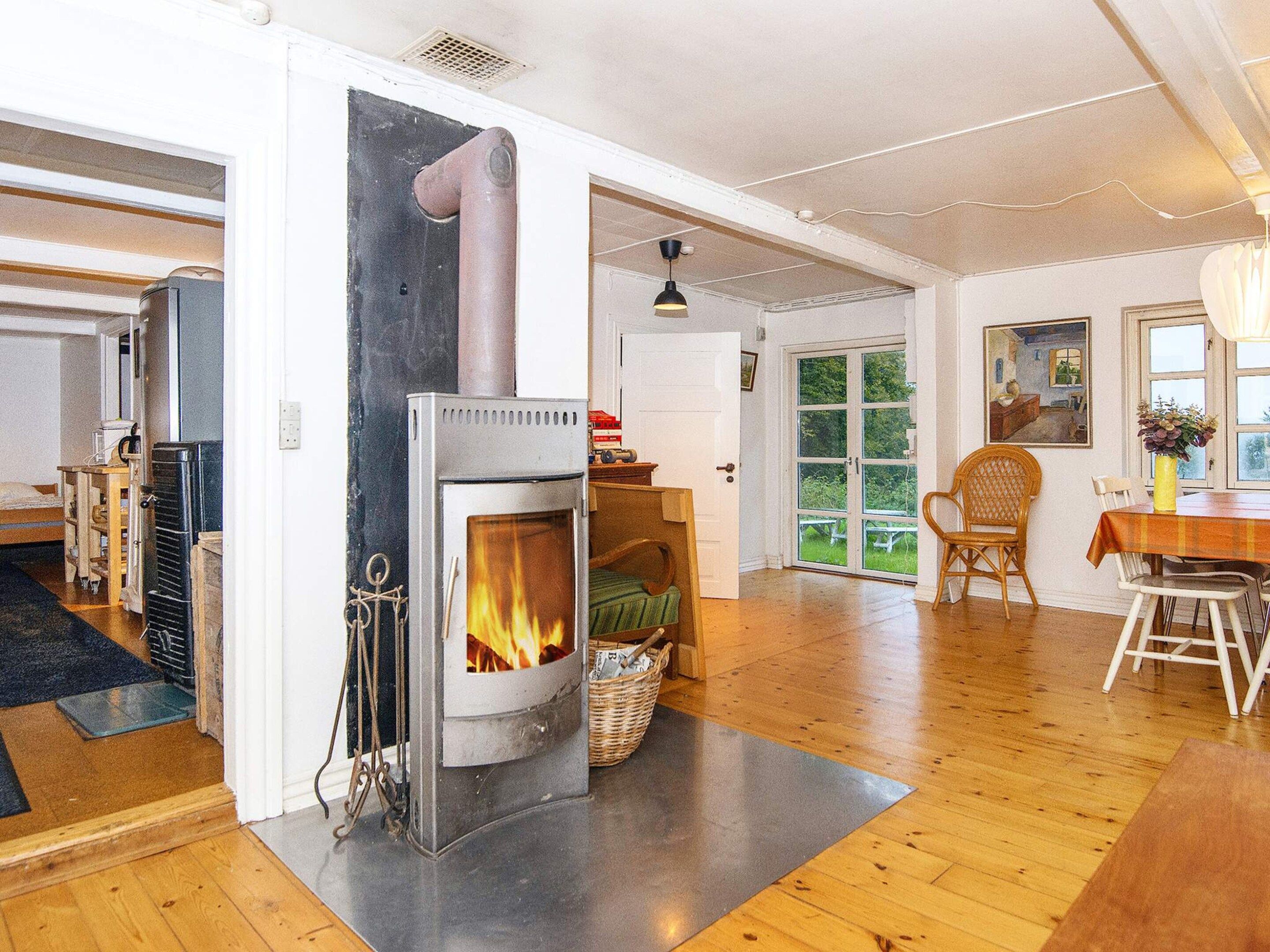 A cozy room with a wood-burning stove, a dining table with chairs, and a view of the outdoors through a glass door.