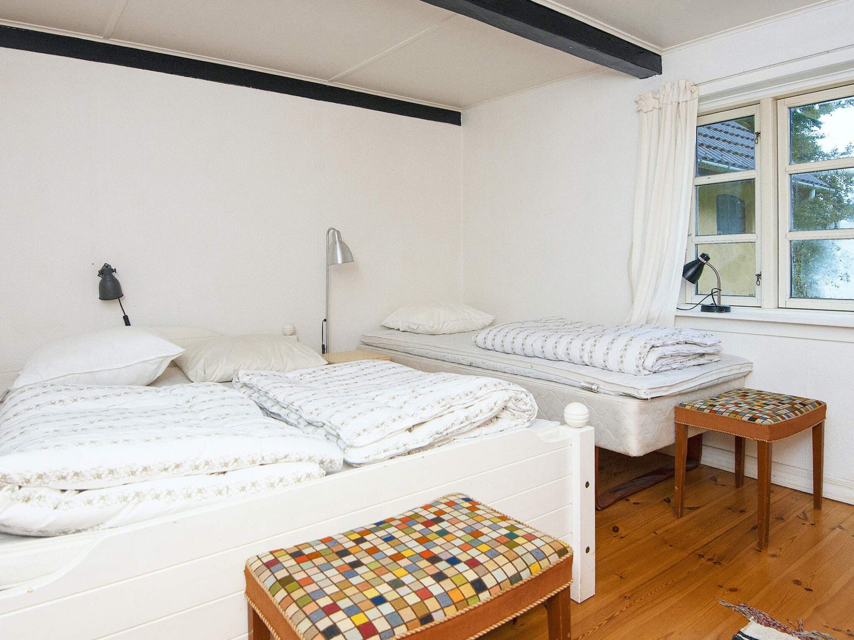 A bedroom with two beds, a small stool, and a window with curtains.