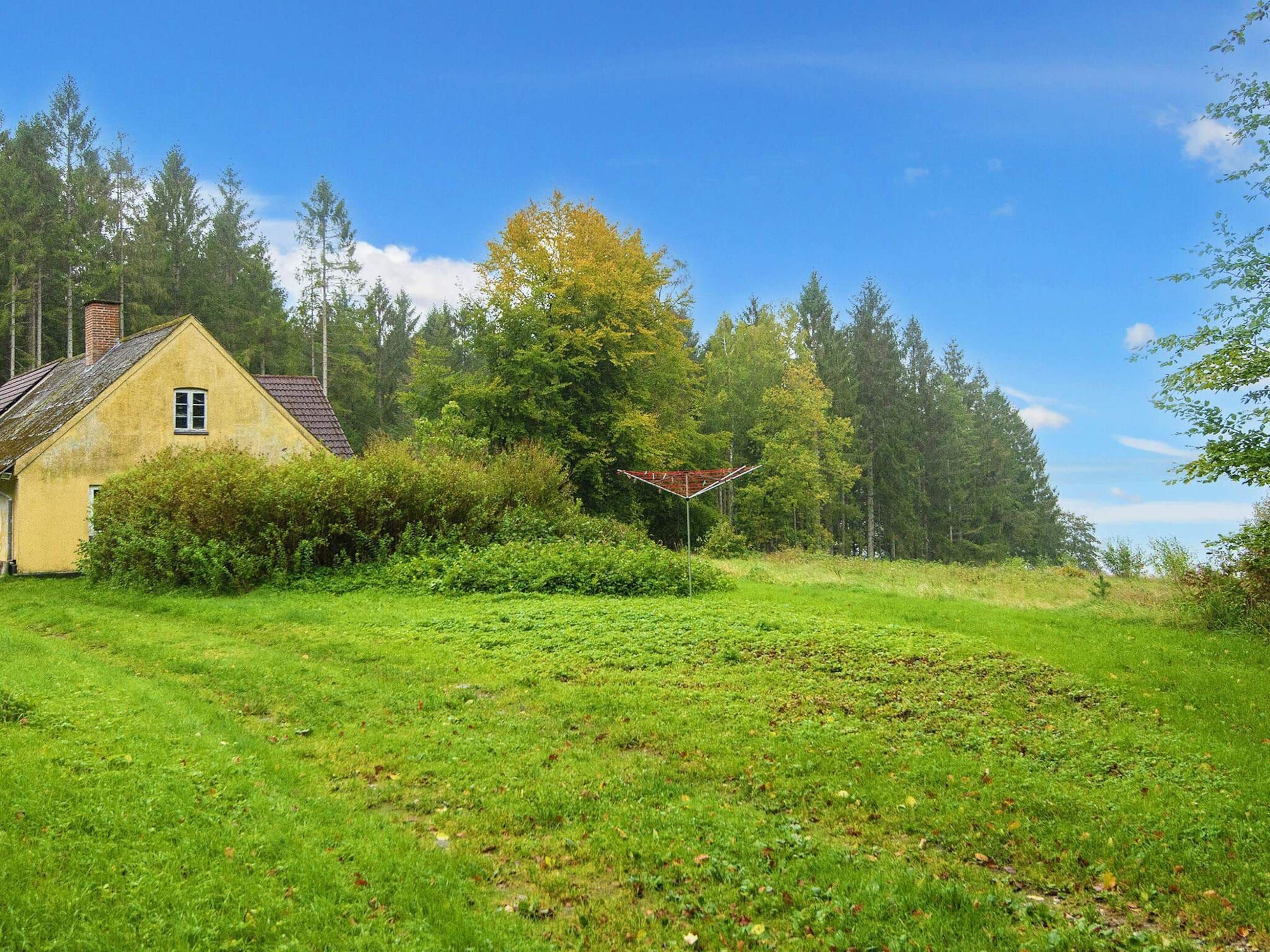 A yellow house with a red roof, surrounded by green grass and trees.