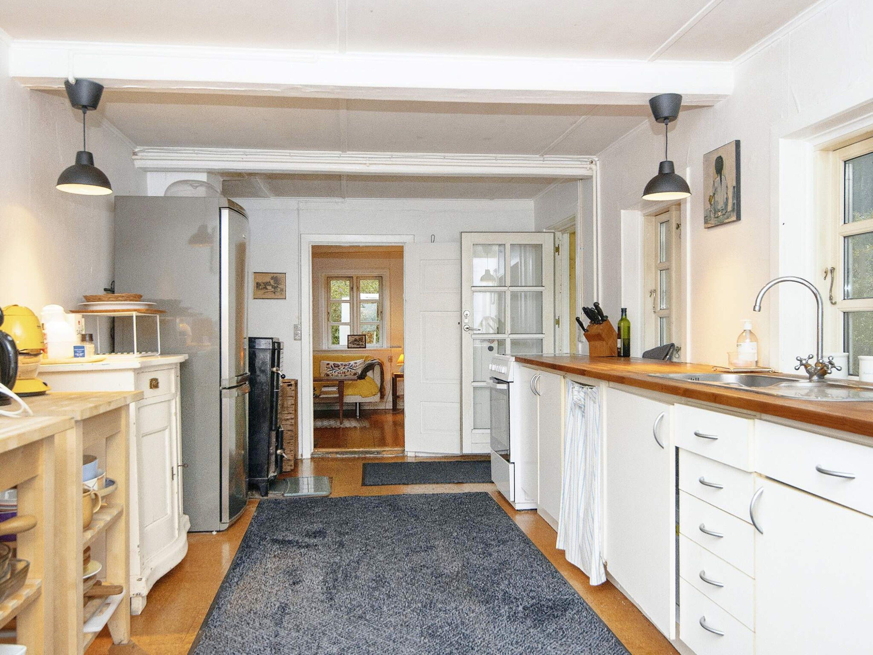 A kitchen with white cabinets, a wooden countertop, and a black rug. There is a dining area in the background with a table and chairs.