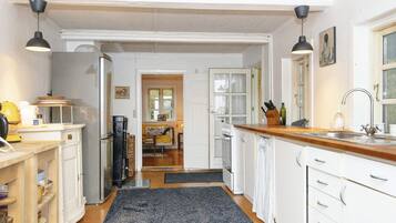 A kitchen with white cabinets, a wooden countertop, and a black rug. There is a dining area in the background with a table and chairs.