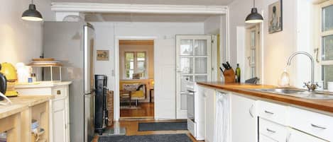 A kitchen with white cabinets, a wooden countertop, and a black rug. There is a dining area in the background with a table and chairs.