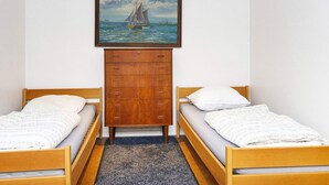 A small, simple room with two wooden beds, a wooden dresser, and a painting of a sailboat on the wall. - 5 Person Holiday Home in Skanderborg (Skanderborg)