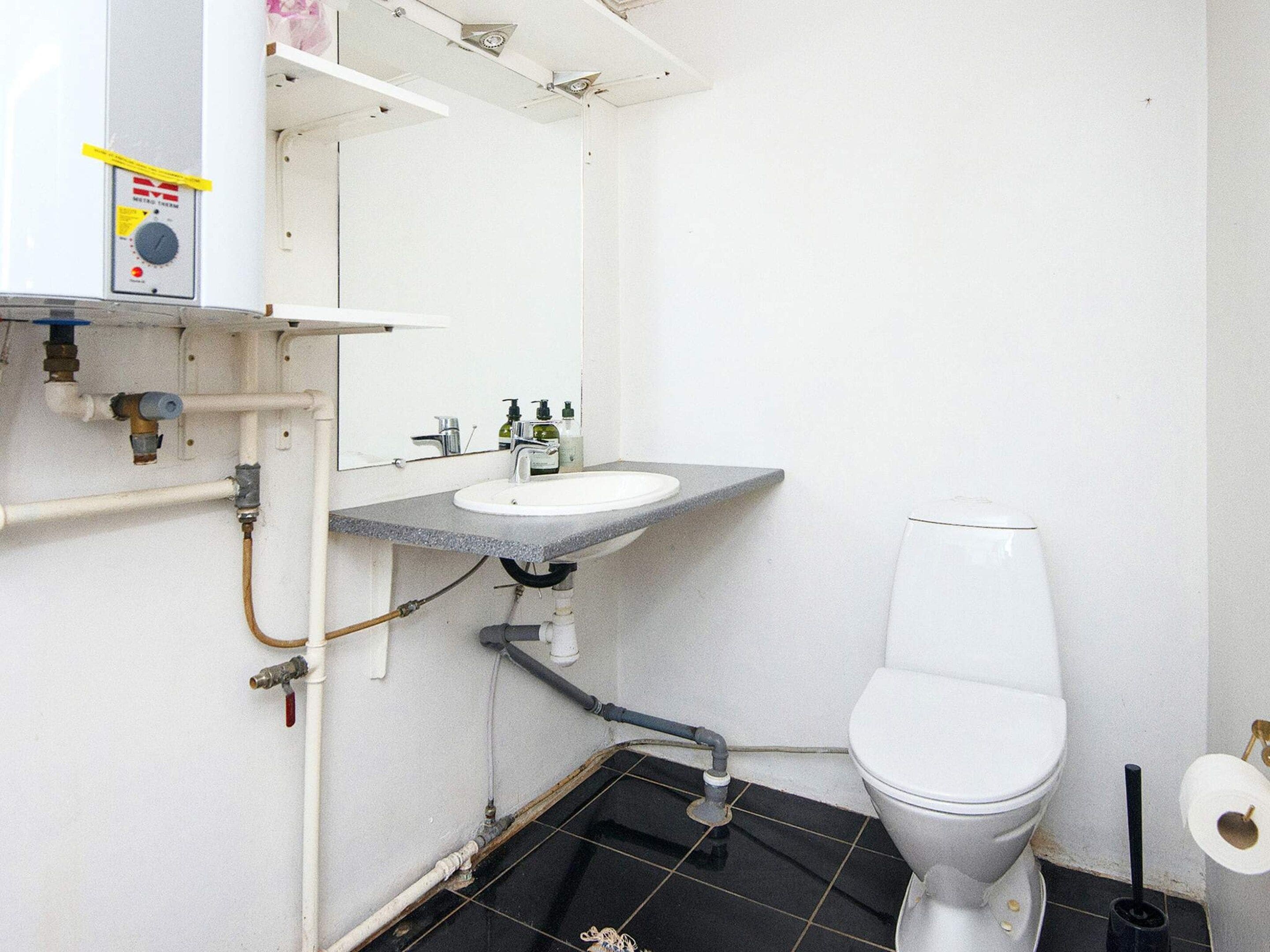 Een badkamer met een wit toilet, een wastafel met spiegel erboven en een wandradiator.