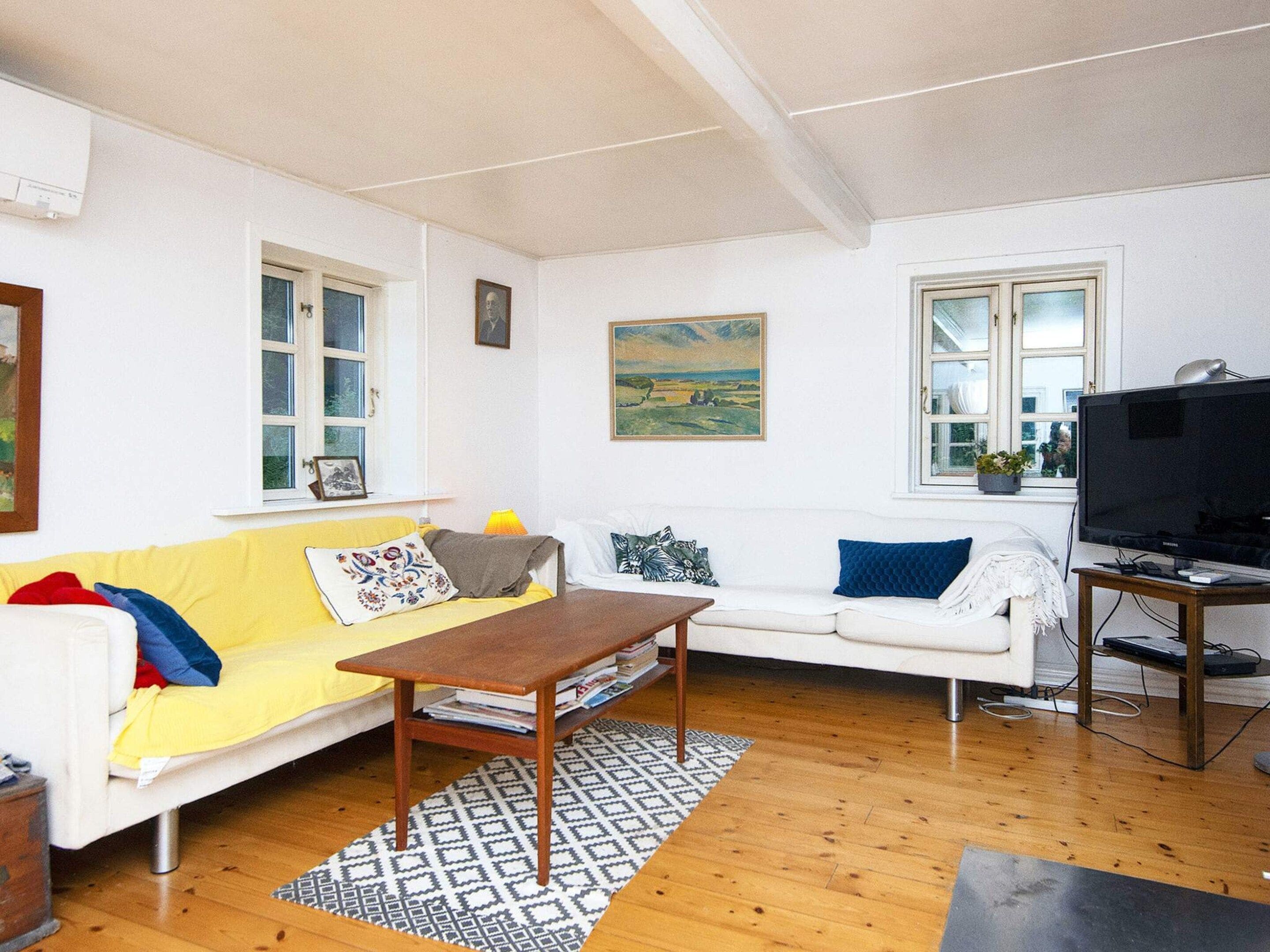 A living room with a yellow sofa, white sofa, wooden coffee table, and a TV on a wooden stand.