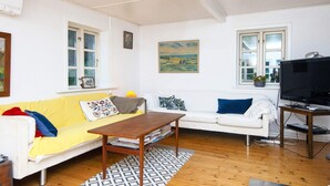 A living room with a yellow sofa, white sofa, wooden coffee table, and a TV on a wooden stand. - 5 Person Holiday Home in Skanderborg (Skanderborg)