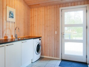 Ett kompakt kök med tvättmaskin, träväggar, ett handfat och en dörr med ett fönster.