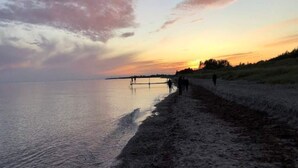 Une plage au coucher du soleil, avec une mer calme, un rivage sablonneux et quelques personnes se promenant le long de la plage.
