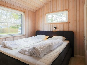 A room with wooden walls, a bed with white bedding, a window, and a wall-mounted light fixture. - 5 Star Holiday Home in Dannemare (Dannemare)