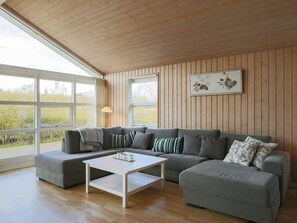 A modern living room with a sectional sofa, a white coffee table, and large windows offering a view of the outdoors. - 5 Star Holiday Home in Dannemare (Dannemare)