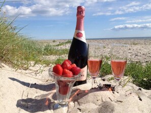 A bottle of champagne, two glasses, and a bowl of strawberries on a sandy beach. - 5 Star Holiday Home in Dannemare (Dannemare)