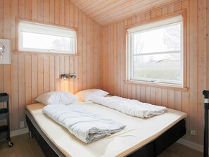 Ett rum med tr äväggar, en säng med vita sängkläder, två fönster och en väggmonterad lampa.