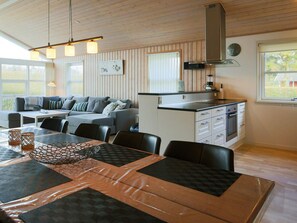 A modern kitchen with a built-in oven, a dining area with a table and chairs, and a living area with a sofa and a coffee table.