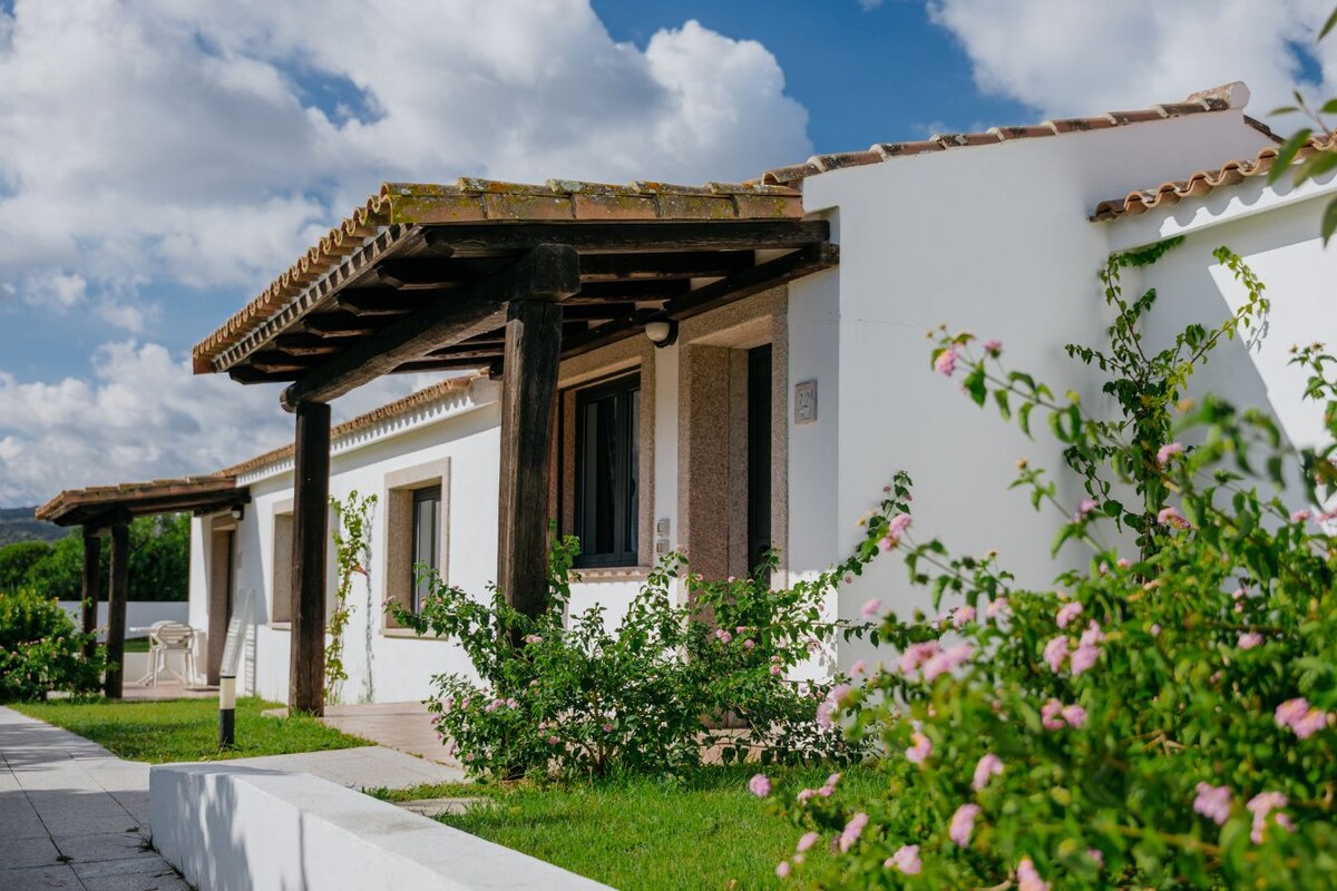 A row of white buildings with tiled roofs, wooden pergolas, and a well-maintained garden with pink flowers.
