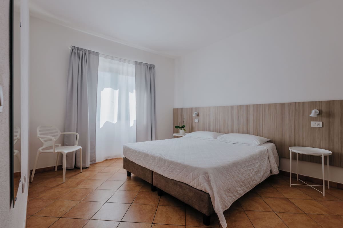 A bedroom with a bed, a chair, a bedside table, and a window with curtains.