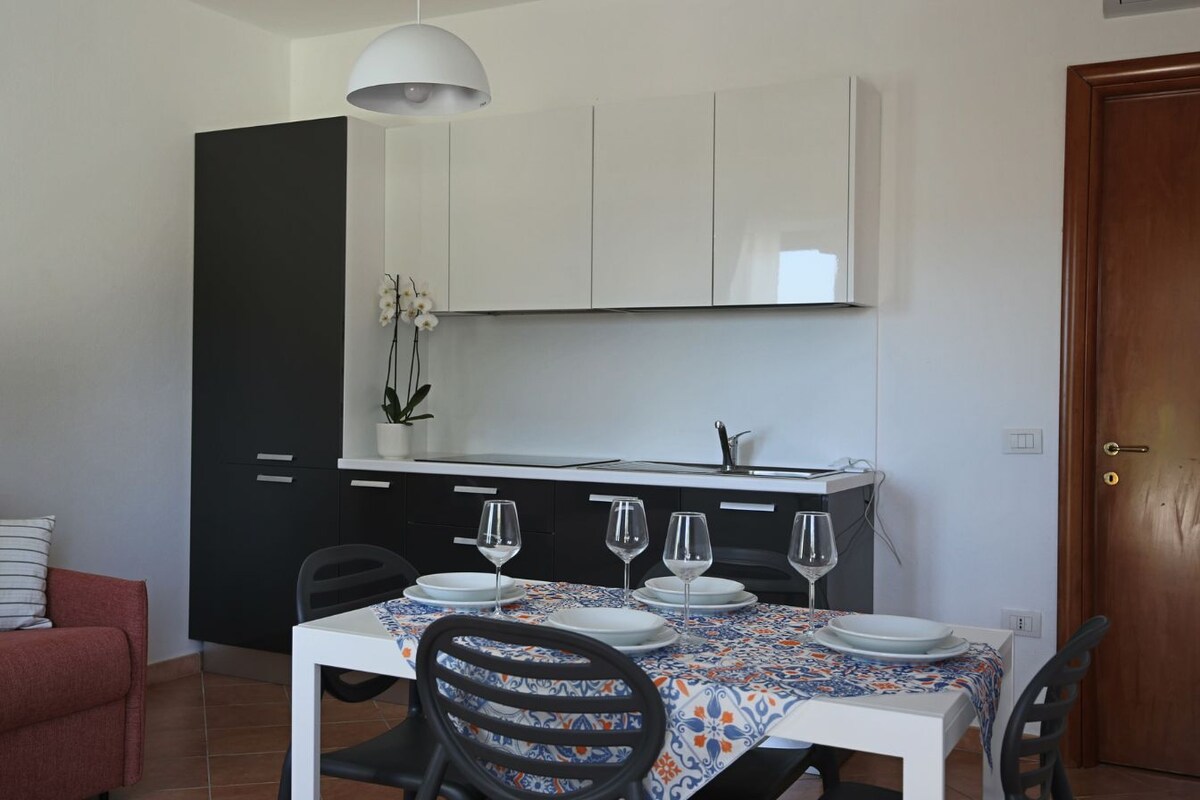 A compact living space with a dining area, kitchenette, and a red sofa with striped cushions.