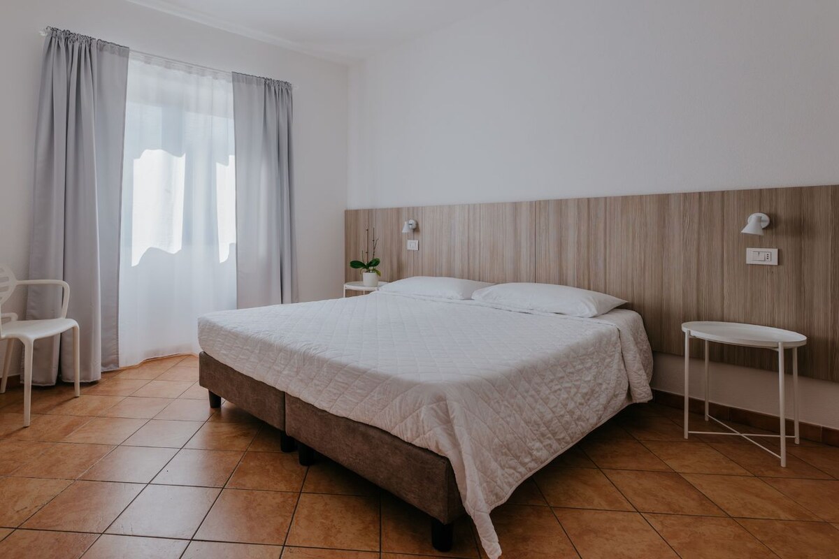 A bedroom with a bed, a bedside table, a chair, and a window with curtains.