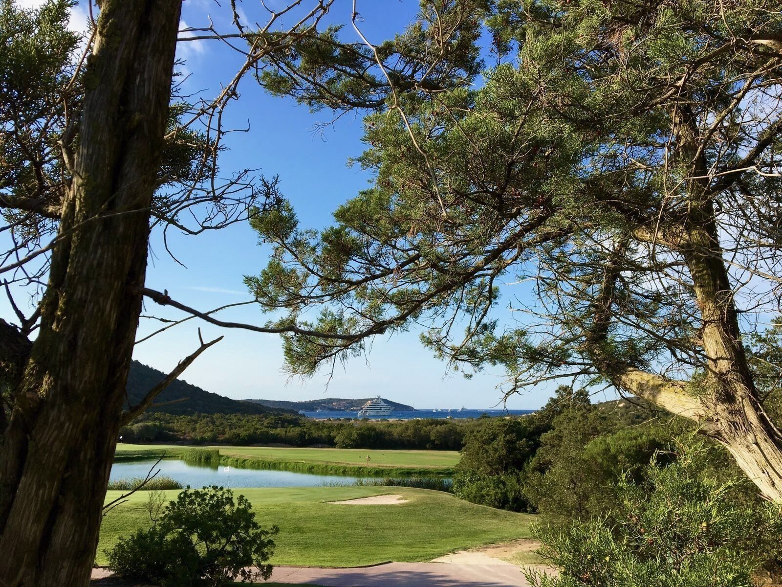 A golf course with a pond, surrounded by trees and hills.