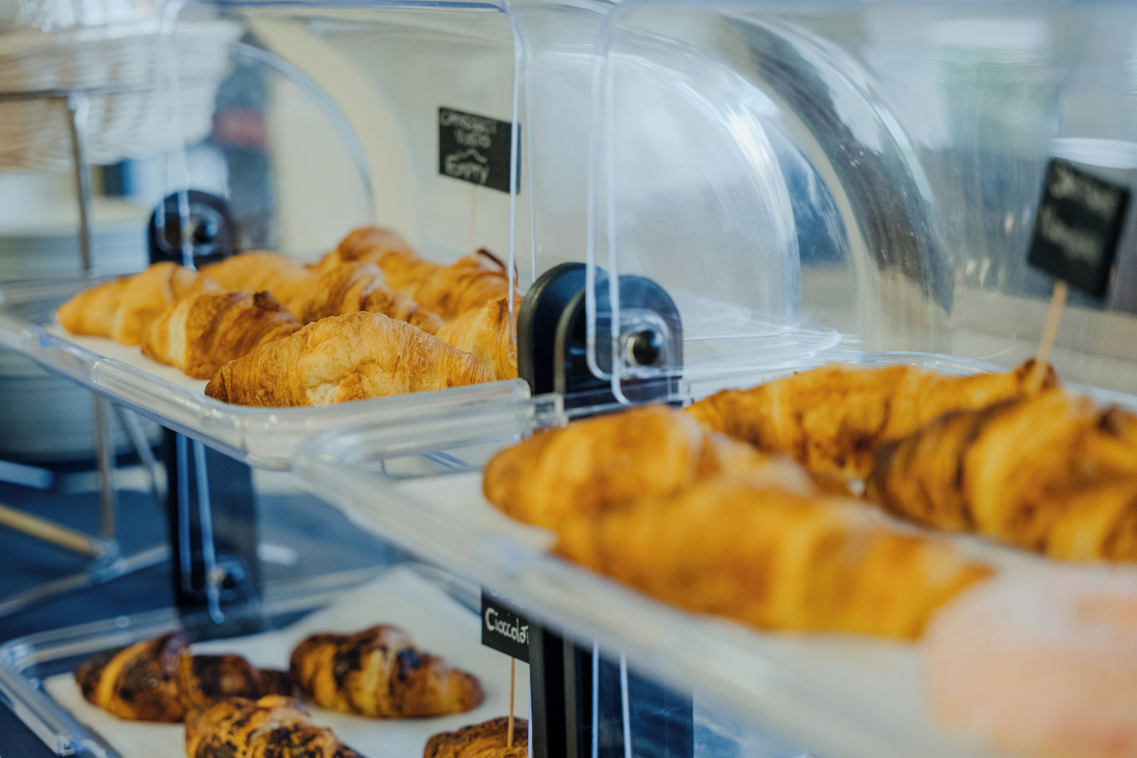 Mostrador de panadería con diversas pastas, incluyendo croissants y magdalenas, cubiertas con plástico transparente.