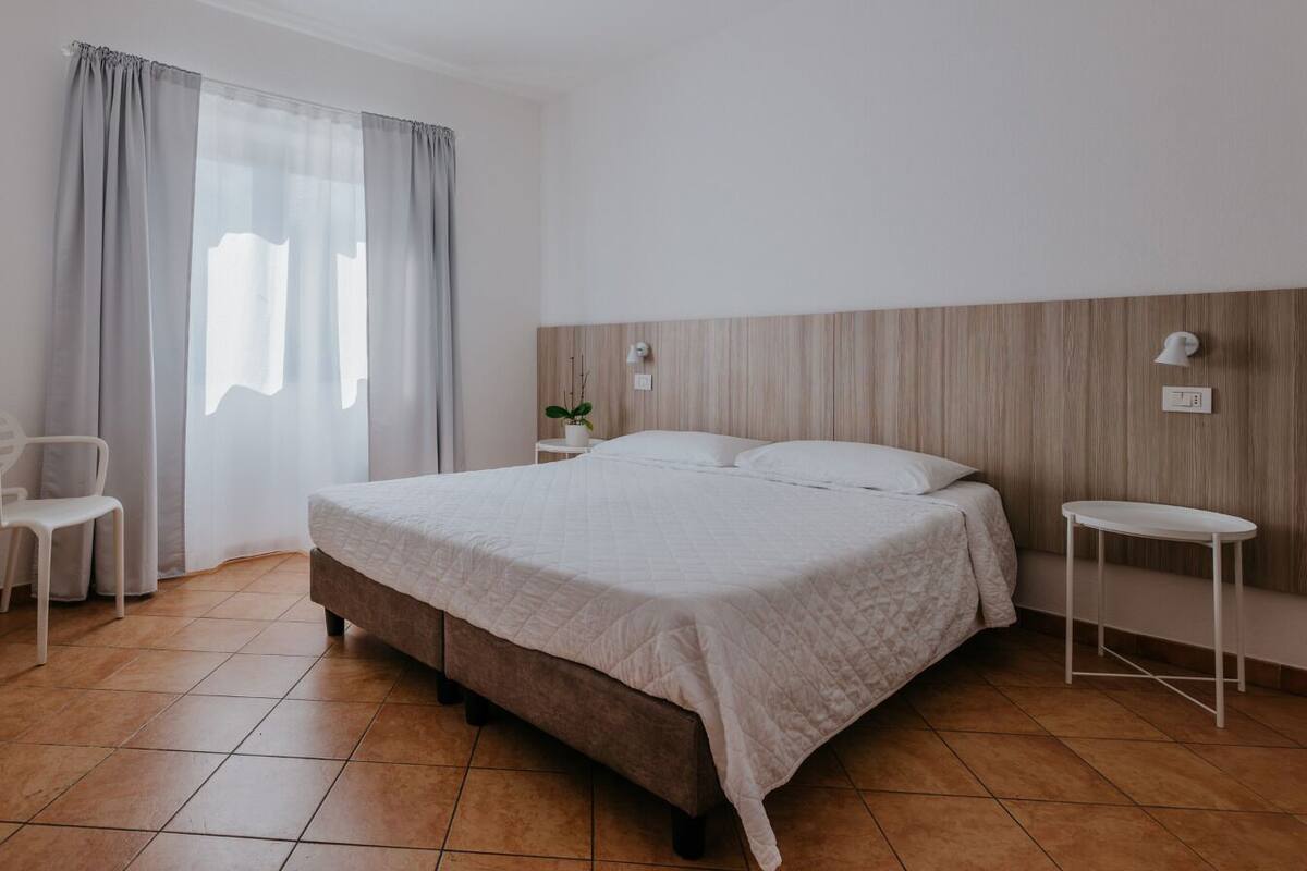 A bedroom with a bed, a bedside table, a chair, and a window with curtains.