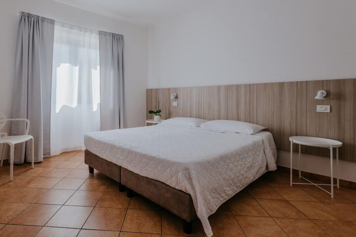 A bedroom with a bed, a bedside table, a chair, and a window with curtains.