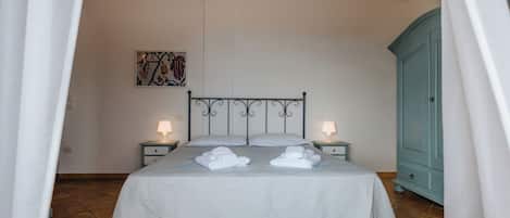 A neatly made bed with white linens and two folded towels, a wall-mounted artwork, and a teal cabinet.
