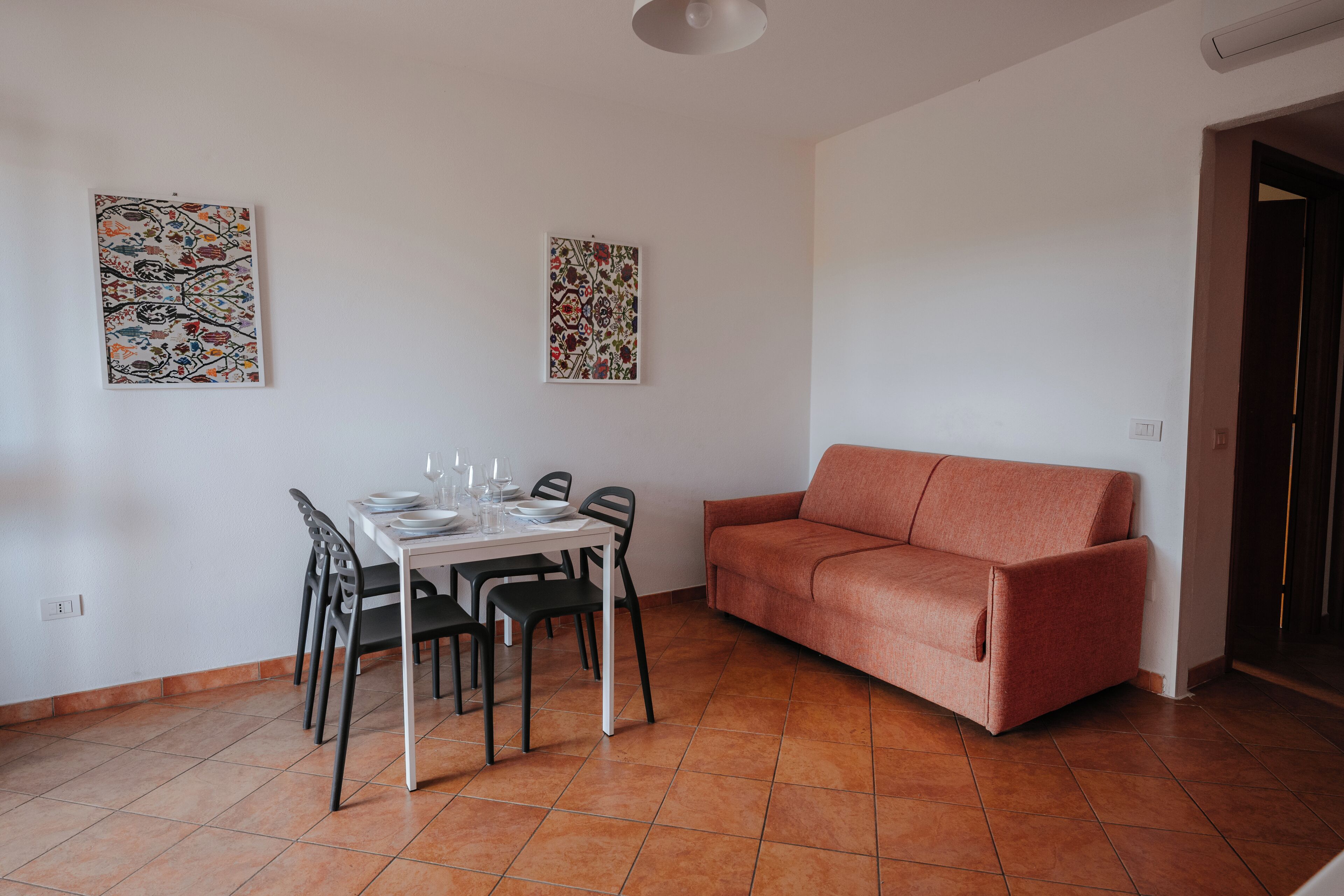 Uma área de refeições com mesa posta para quatro pessoas, duas obras de arte na parede e um sofá vermelho.