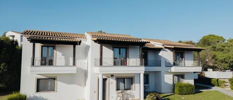 A two-story building with a tiled roof, balconies, and a small garden area.