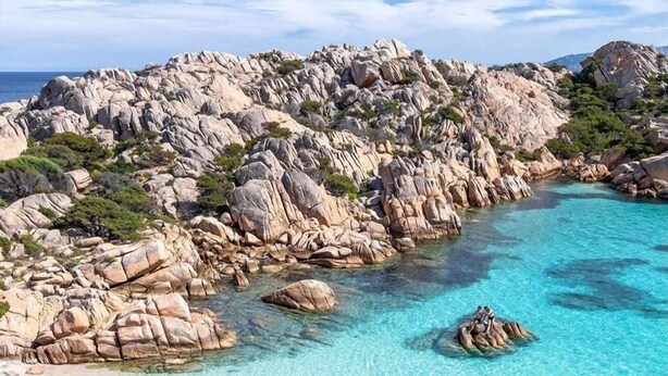 A rocky coastline with clear turquoise water, a sandy beach, and a few people swimming. - La Smeraldina Resort (Santa Teresa di Gallura)