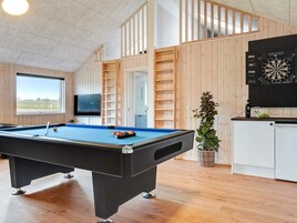 Una mesa de billar con dardos y una televisión en una habitación con paredes de madera y un ventanal.
