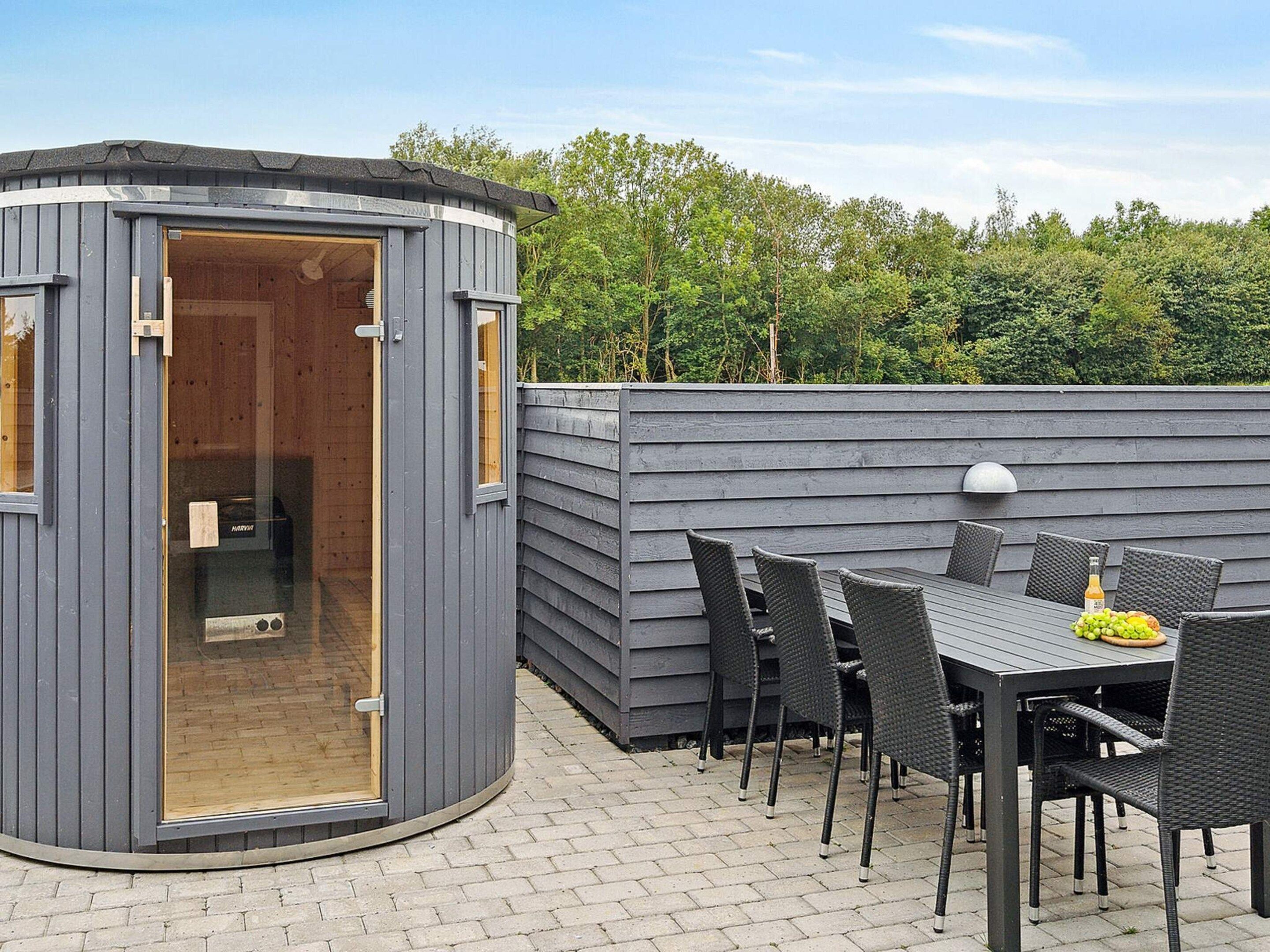 A small, modern outdoor room with a built-in bench and a table, surrounded by a wooden fence.